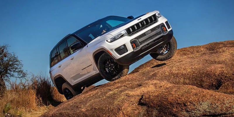 White Jeep Grand Cherokee Trailhawk ascending a steep, rocky hill, showcasing its off-road capability.