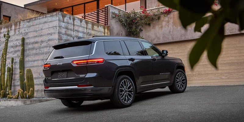 The rear-left view of a dark gray Jeep Grand Cherokee with brake lights on, parked on a paved driveway.