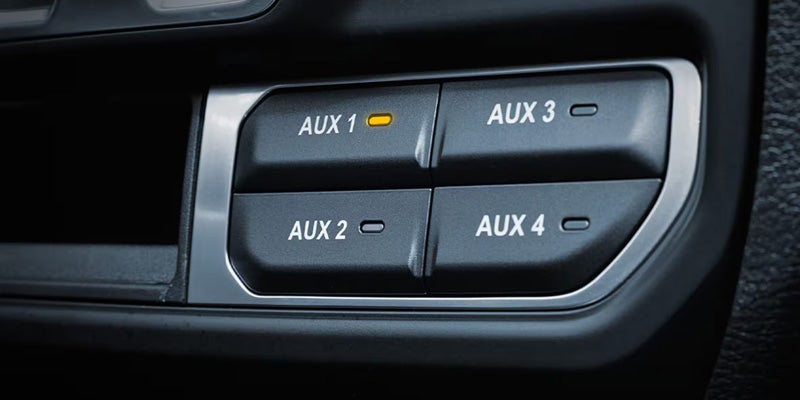 A set of four black auxiliary rocker switches, AUX 1 through AUX 4, mounted flush in a black console. AUX 1 glows orange.