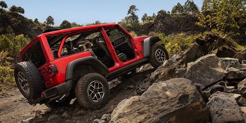 Red Jeep Wrangler Rubicon, with doors and roof removed, off-roading up a rocky hill.