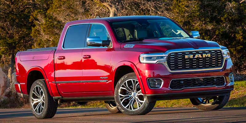 A shining red Ram pickup truck with chrome accents including the RAM logo on the grille, parked on the road.