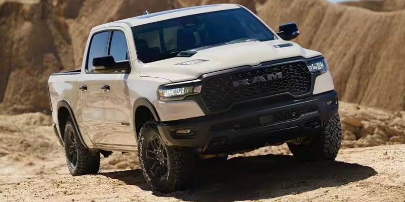 A light-colored Ram pickup truck on a sandy, off-road terrain with a steep dirt embankment in the background.