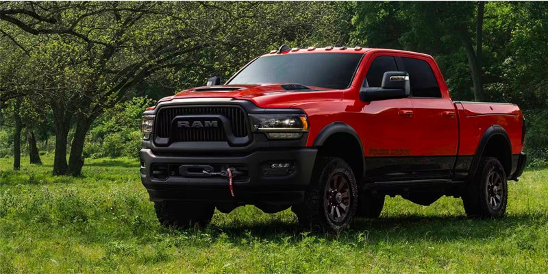 Front view of a red Ram Power Wagon pickup truck parked in a grassy field with trees in the background.
