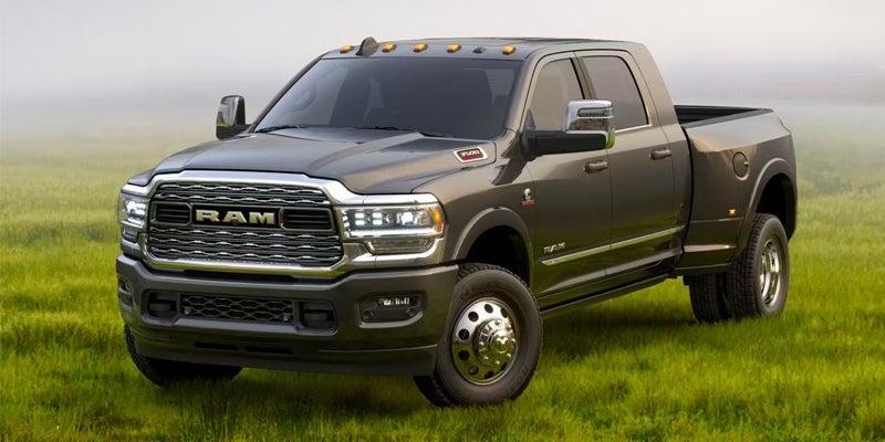 A dark gray Ram 3500 pickup truck with dual rear wheels parked in a field of green grass with hazy sky.