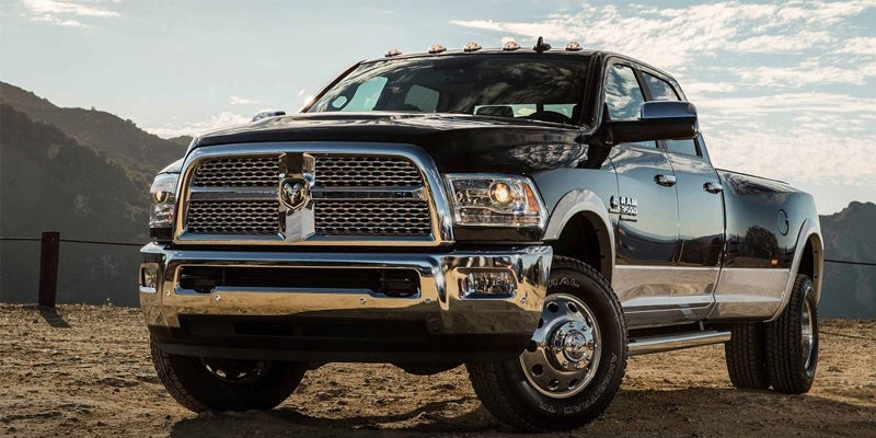 A black 2013 Ram 3500 heavy-duty pickup truck with chrome grille and bumper on a dirt road, mountains in background.