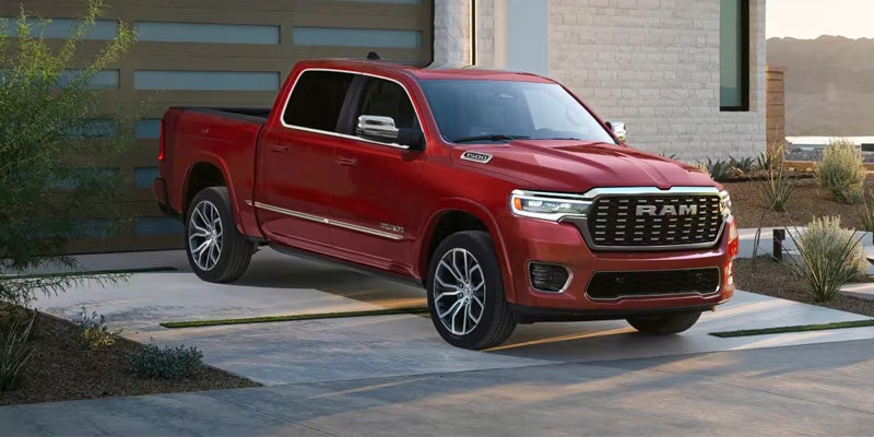 A red Ram 1500 truck with a chrome grille is parked on a concrete driveway in front of a modern house.