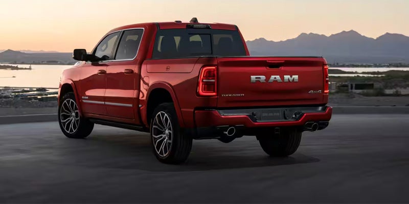 Rear view of a red Ram pickup truck with mountains and a body of water in the background.