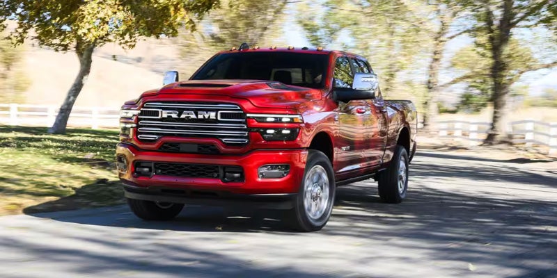 A glossy red 2023 Ram 2500 Limited Longhorn pickup truck at an angle on an asphalt road.