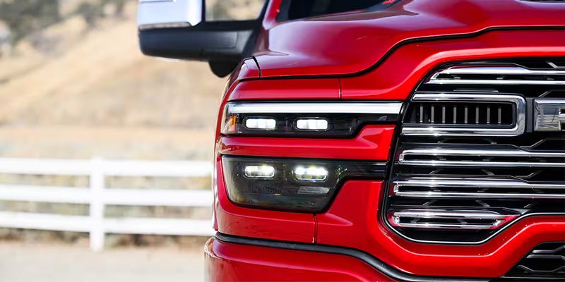 Close-up of the front right quarter of a red pickup truck, showing headlight, grille, and part of the side mirror.
