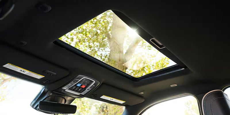 Sunlight shines through the open sunroof of a car, illuminating a black fabric ceiling.