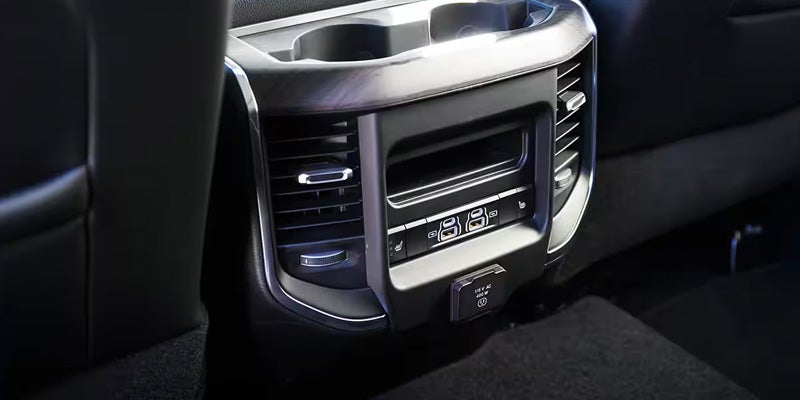 Rear passenger console in a vehicle with two cupholders, air vents, USB ports, power outlet, and seat heater buttons.