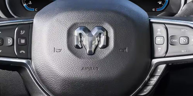 Close-up of a Dodge Ram steering wheel with controls and the Ram logo.