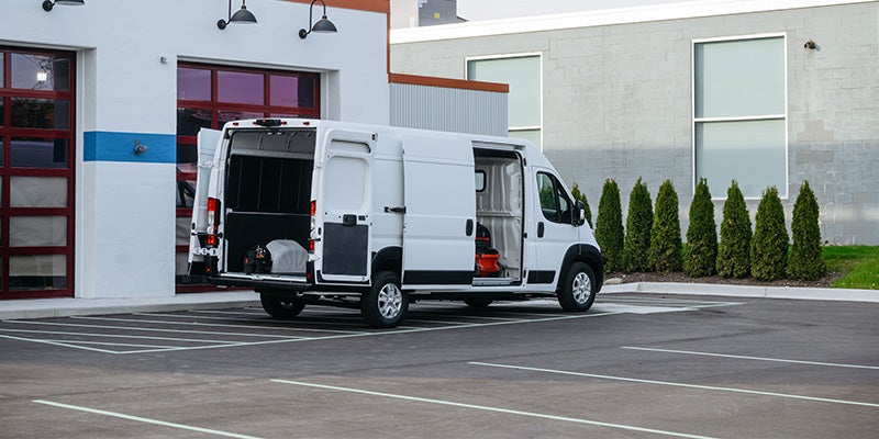 White delivery van with all its doors open, parked in a lot next to a white and blue building.