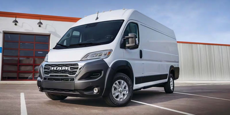 A spacious white Ram ProMaster van with a black grille and bumper is parked in front of a building.