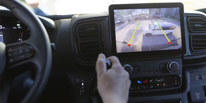 A dashboard view from the driver's perspective, showing a hand on the shifter, and a backup camera display.